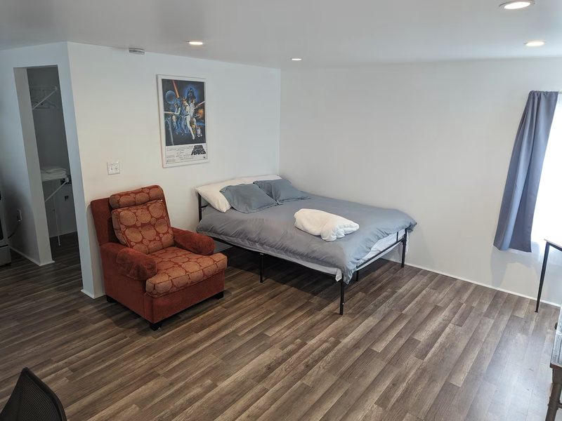 The sleeping area with an armchair and a closet nook, blackout curtain drawn at the window.