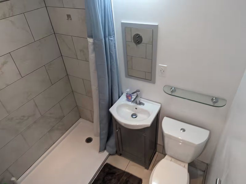 Bathroom with a tiled step-in shower, vanity and glass shelf.